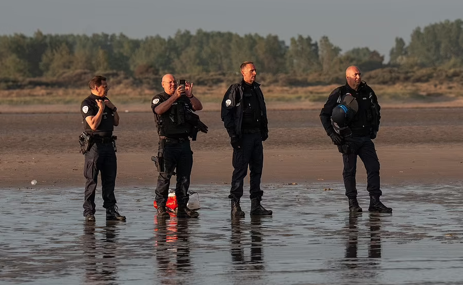 French police stand back and watch as migrant families including small children pack themselves onto small boats heading across the Channel to the UK